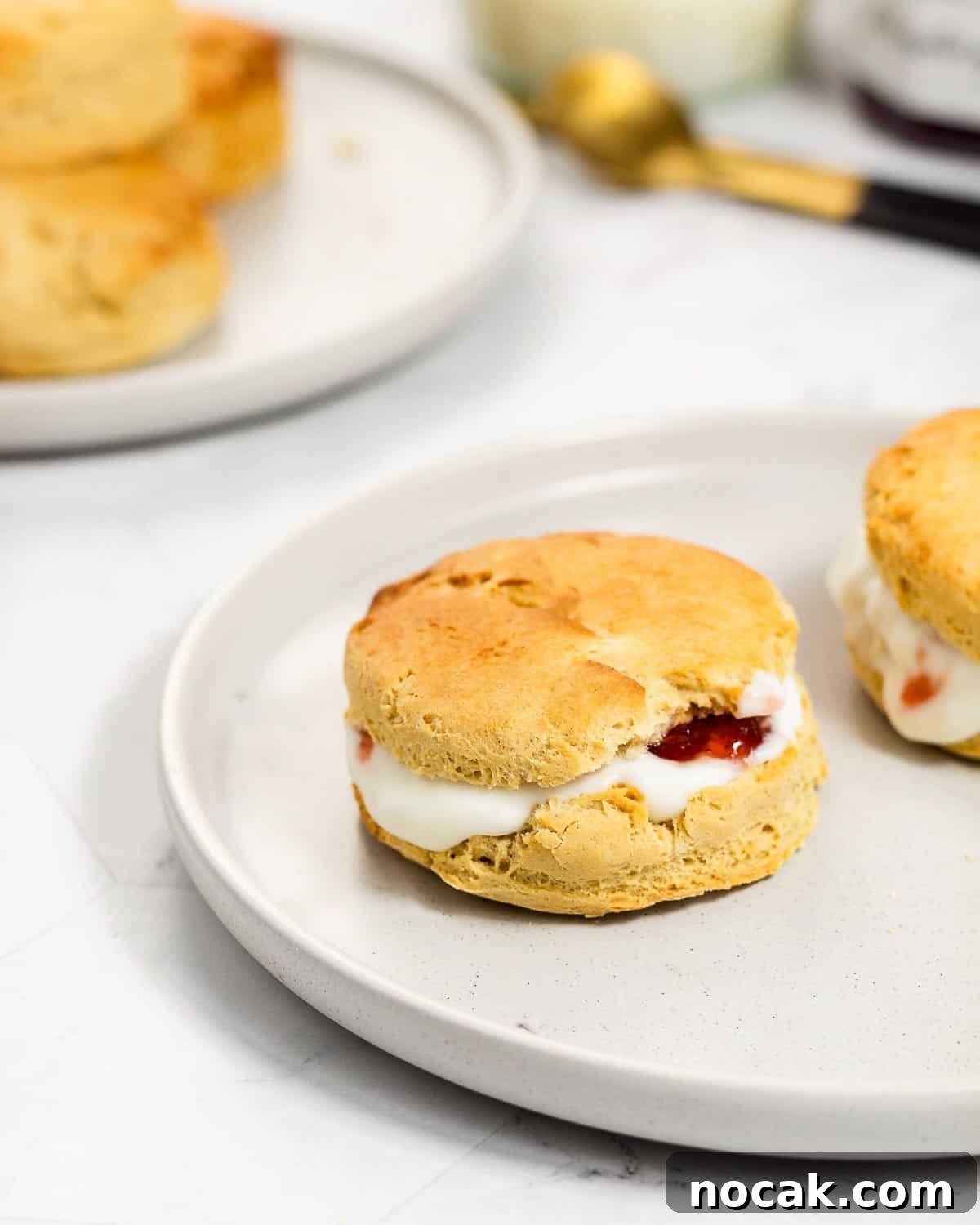 4-Ingredient Protein Scones Made Without Butter 2 Two scones with yoghurt and jam on a grey plate. In the background there is a plate with some more scones.