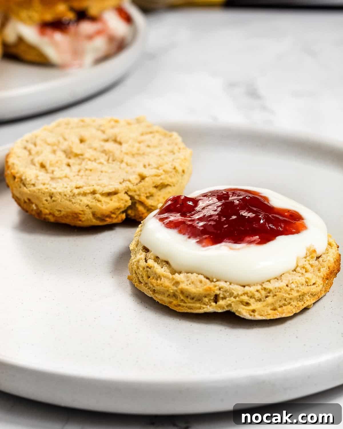 4-Ingredient Protein Scones Made Without Butter 9 A scone cut open on a grey plate, topped with yoghurt and strawberry jam on one half..