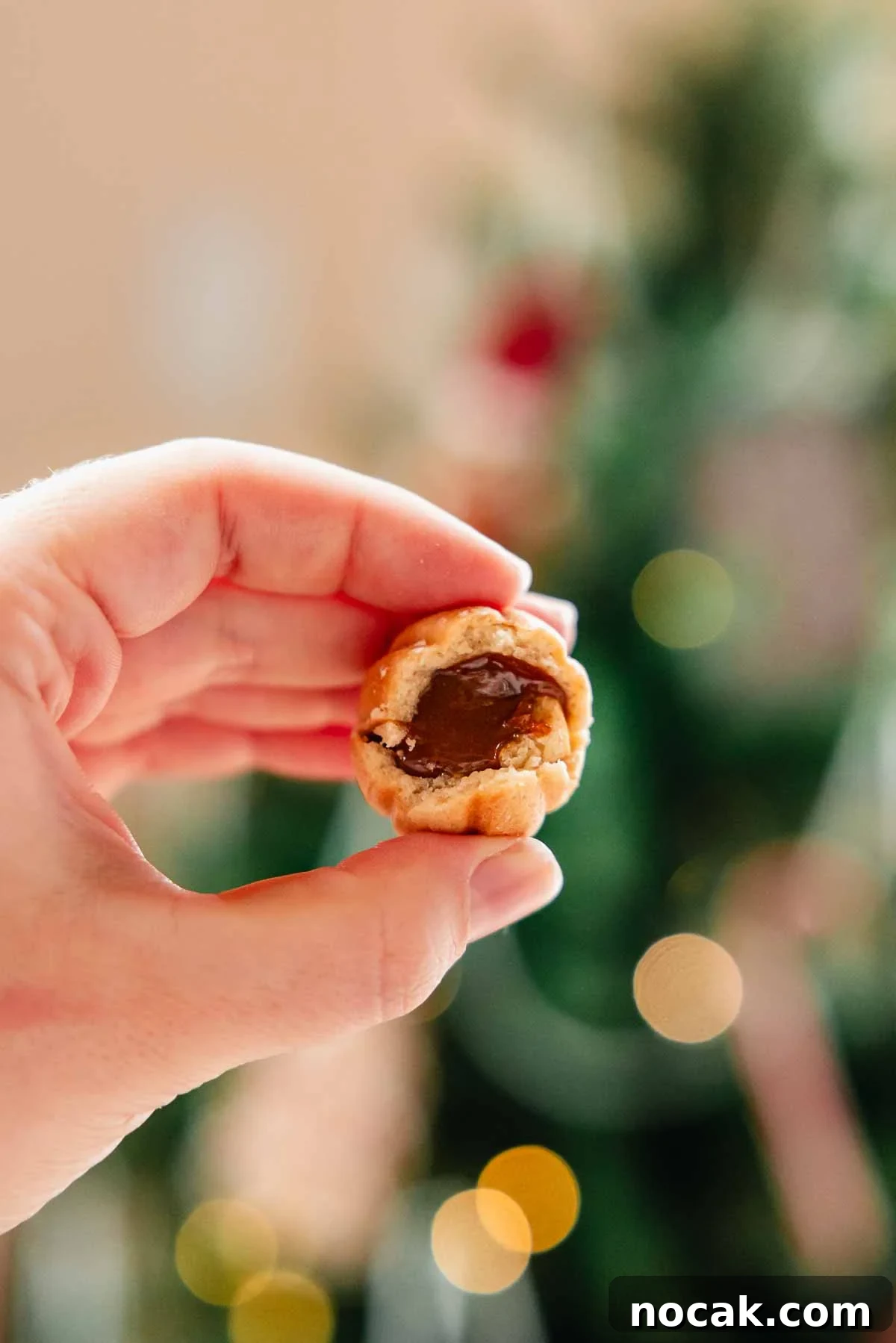 Oreshki Walnut Cookies Recipe — Russian Fillable Pastry Treats 13 holding up a bitten walnut cookie that is filled with dulce de leche
