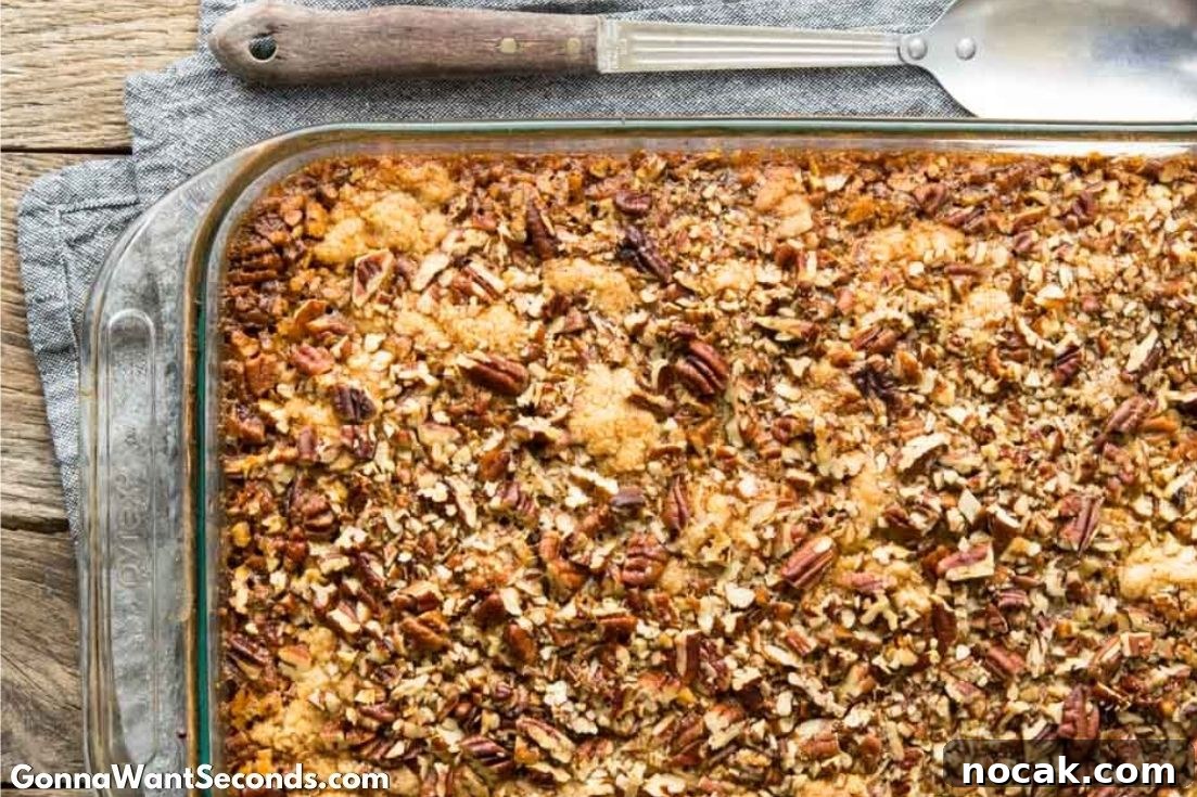 Pecan Pie Cobbler brings together the ooey gooey filling of pecan pie with the decadent cake-like topping of your favorite cobbler! It’s to die for delish! #Pecans #PecanPie #Cobbler #Dessert Pecan Pie Cobbler in a casserole dish with kitchen spoon on the side