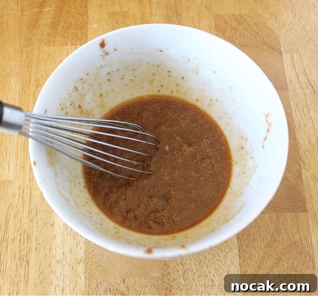 Fudgy Dark Chocolate Cookies — Nut Free Recipe 7 Whisking a brown mixture in a small white bowl.