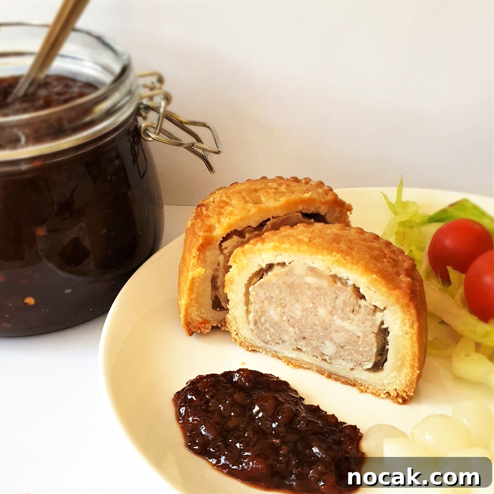A slice of pork pie on a plate alongside a spoonful of Mrs Balls chutney.
