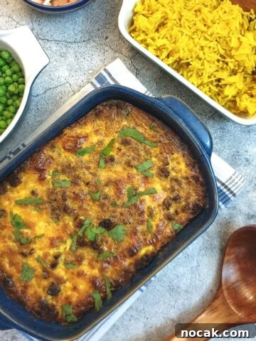 A blue serving dish of bobotie next to a bowl of yellow rice and a bowl of peas.