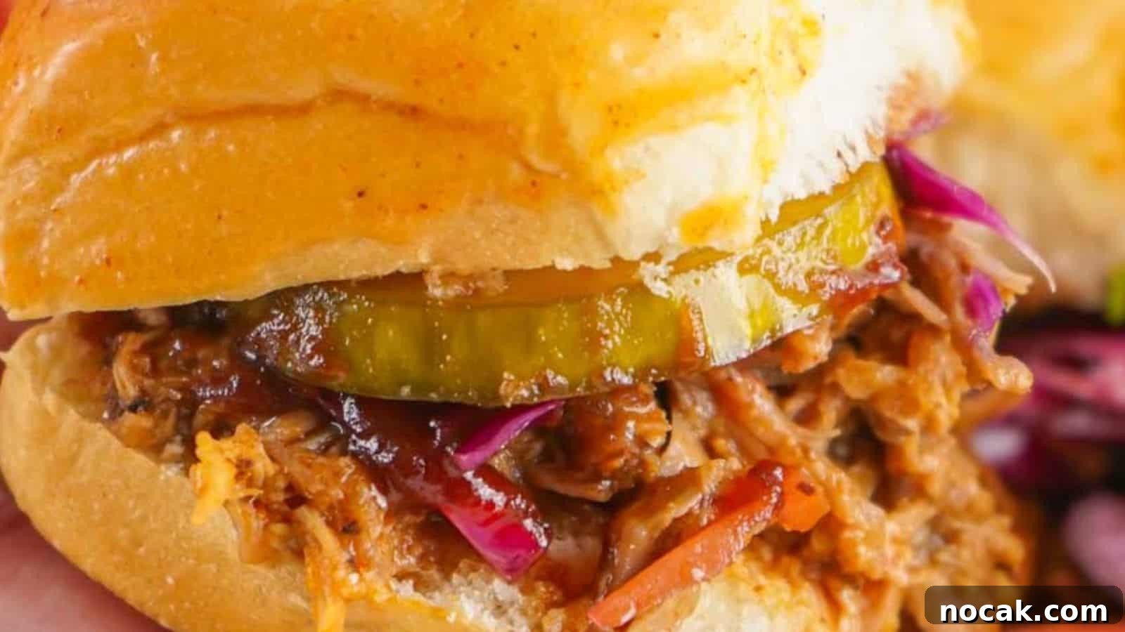 23 Crowd-Pleasing Cookout Recipes for Memorial Day Weekend 24 Close-up of a pulled pork sandwich with pickles and red cabbage on a bun, held in hand, with chips in the background.