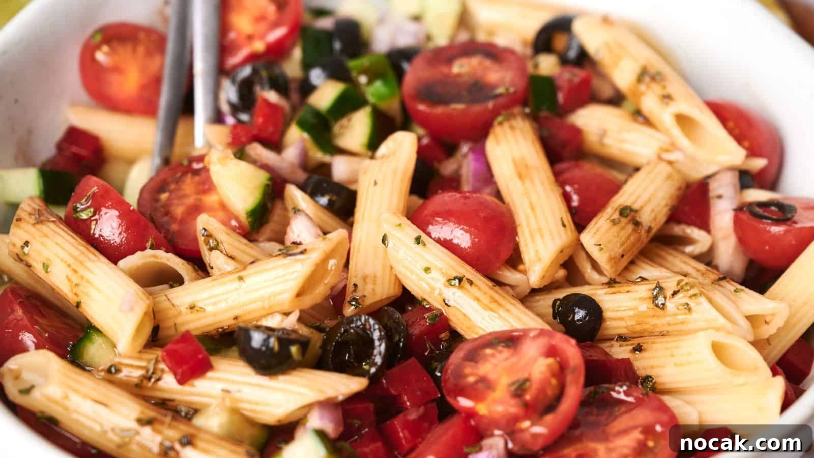 23 Crowd-Pleasing Cookout Recipes for Memorial Day Weekend 25 A bowl of vibrant pasta salad with penne, cherry tomatoes, black olives, diced cucumbers, red onions, and a drizzle of dressing.