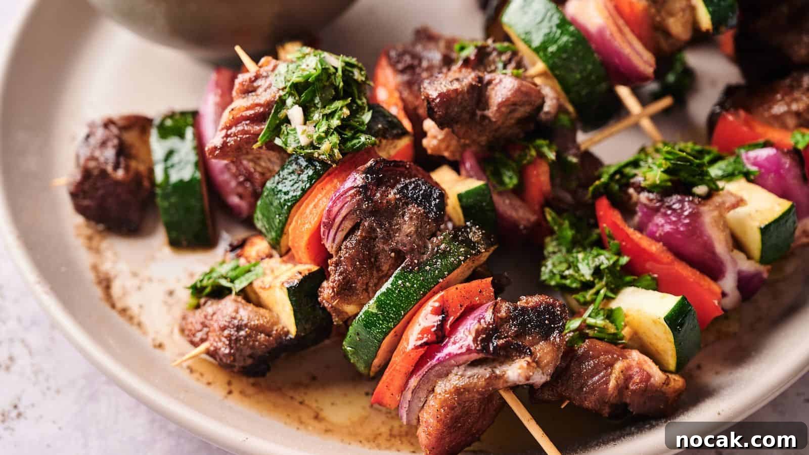 23 Crowd-Pleasing Cookout Recipes for Memorial Day Weekend 6 Grilled meat and vegetable skewers with zucchini, red onion, and red bell pepper, garnished with chopped herbs, served on a beige plate.