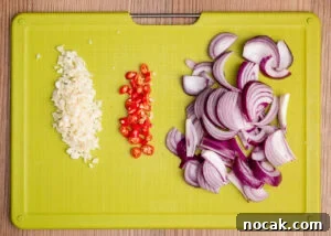 Saag Bhaji Recipe: Creamy Indian Spinach Curry with Spices 5 Chopped red chillies , chopped garlic and sliced red onion on a green chopping board