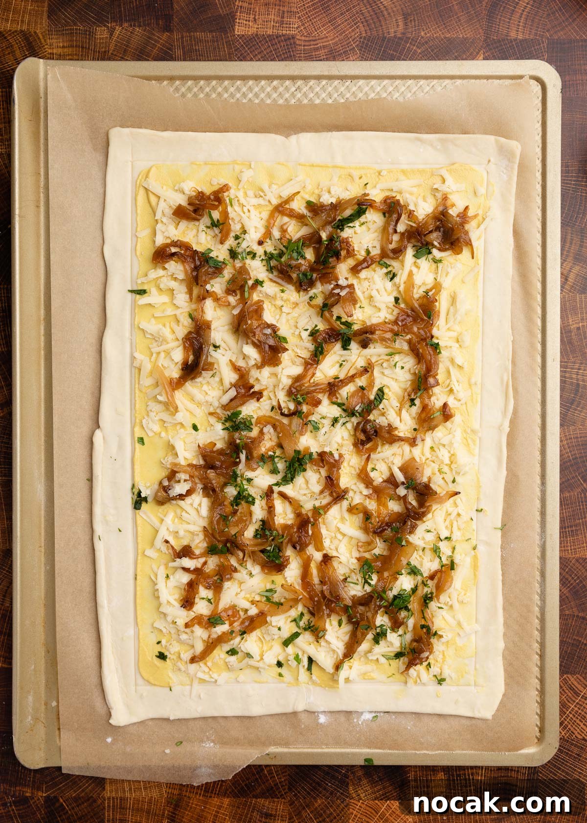 Crispy Puff Pastry Tomato Tart with Herbed Goat Cheese 8 overhead photo of puff pastry on a parchment lined baking sheet, topped with Dijon, shredded gruyere, caramelized onions, and herbs