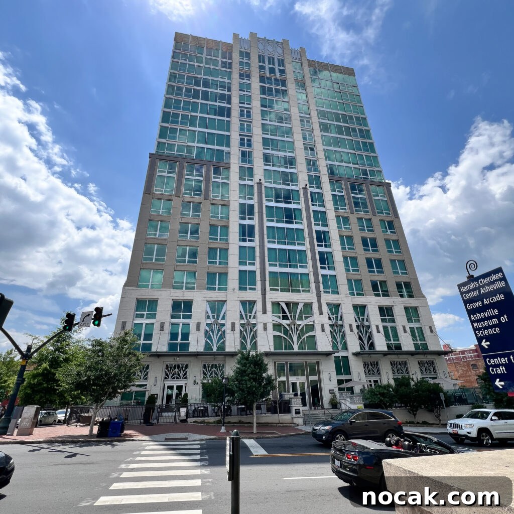 A tall, modern building with green-tinted windows stands on a city street corner under a partly cloudy, romantic sky, with cars parked and a crosswalk in the foreground.