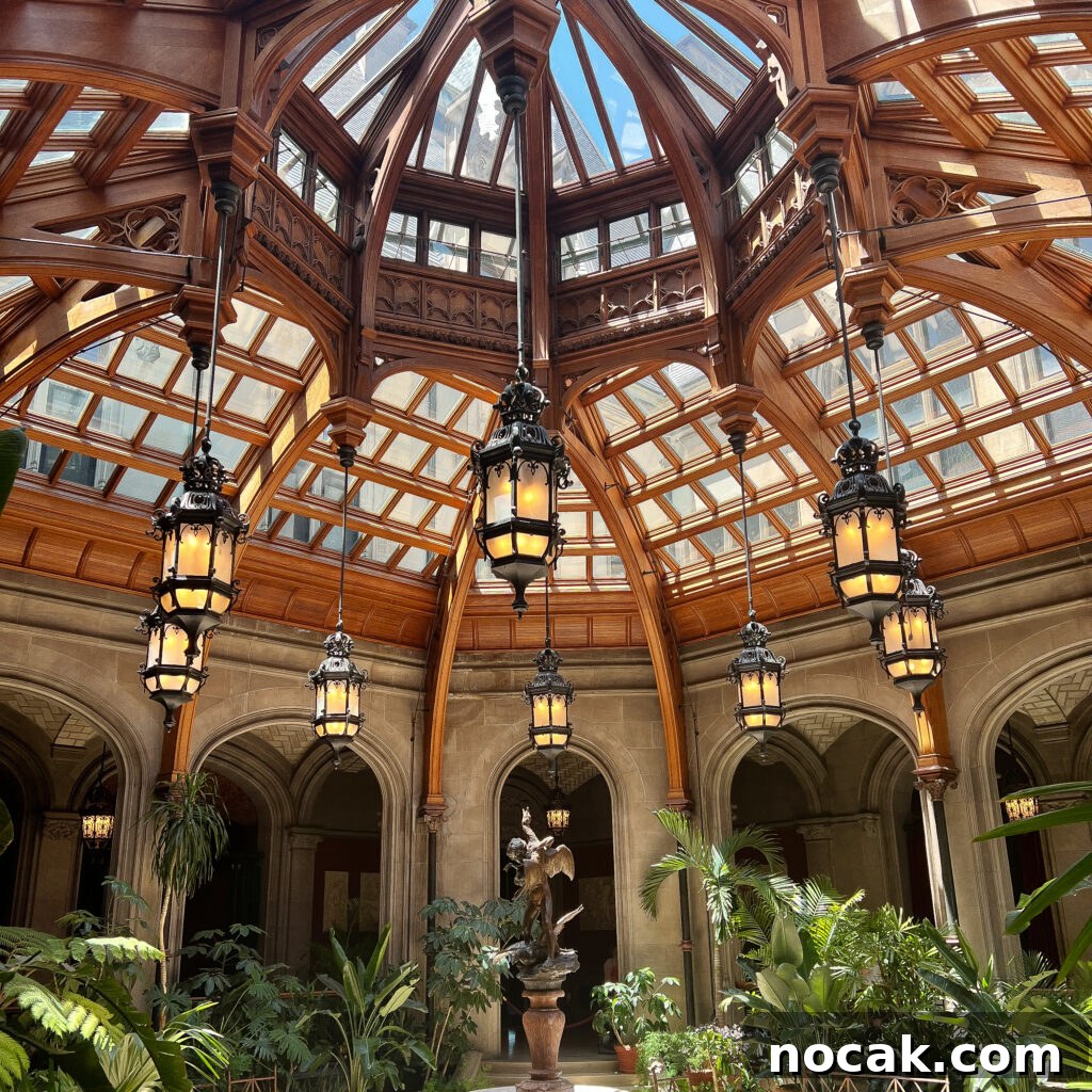 An ornate glass and wood dome ceiling with five romantic vintage lanterns hangs above a lush indoor garden and central statue, all surrounded by arched doorways and classical architecture.