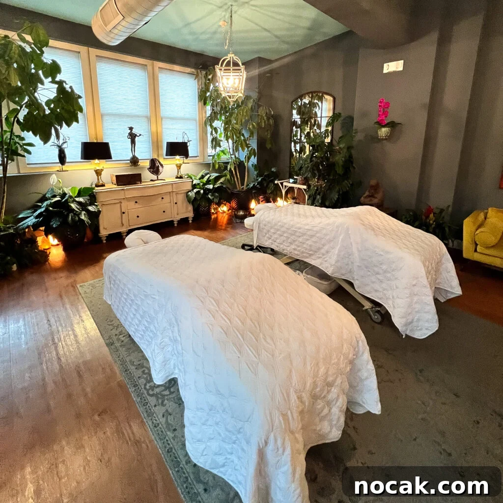 A cozy, romantic spa room with two massage tables covered in white quilts, surrounded by plants, soft lighting, and decorative accents creates a relaxing atmosphere.