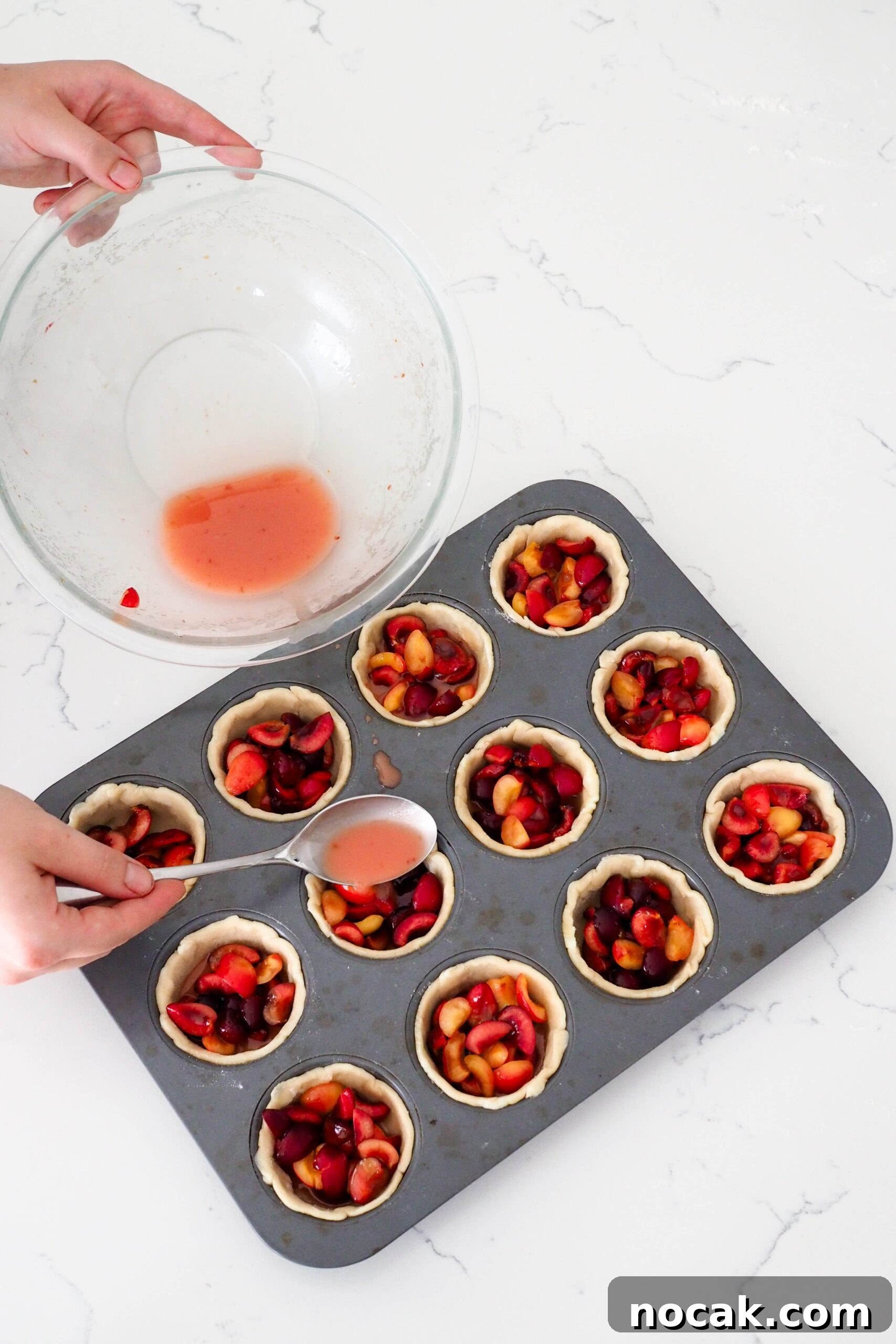 Mini Cherry Pies Recipe: Perfect Bite-Sized Cherry Hand Pies 9 A hand uses a tablespoon to add pink liquid to mini cherry pies.