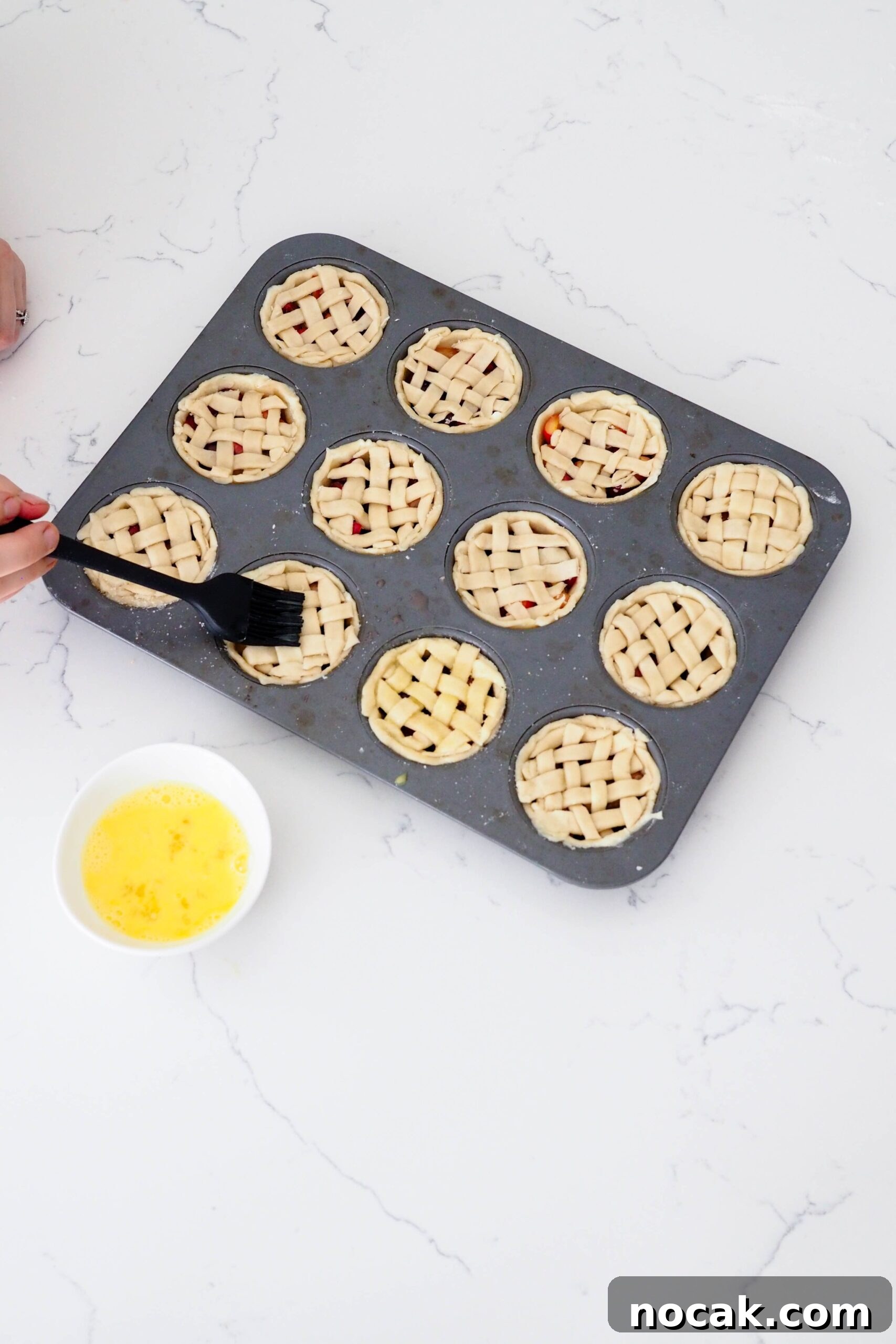 Mini Cherry Pies Recipe: Perfect Bite-Sized Cherry Hand Pies 12 A hand uses a silicone pastry brush to brush egg wash onto mini latticed pies.
