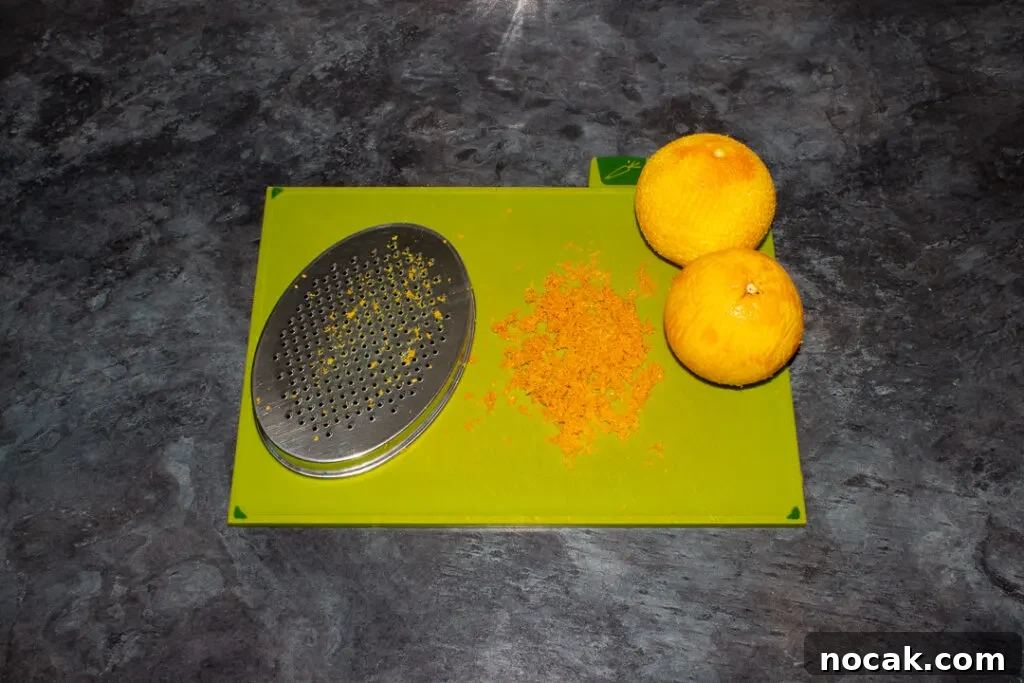 Sticky Orange Glaze Cake Recipe with Zesty Citrus Flavor 10 Two zested oranges, the zest and a grater on a green chopping board on a kitchen worktop.