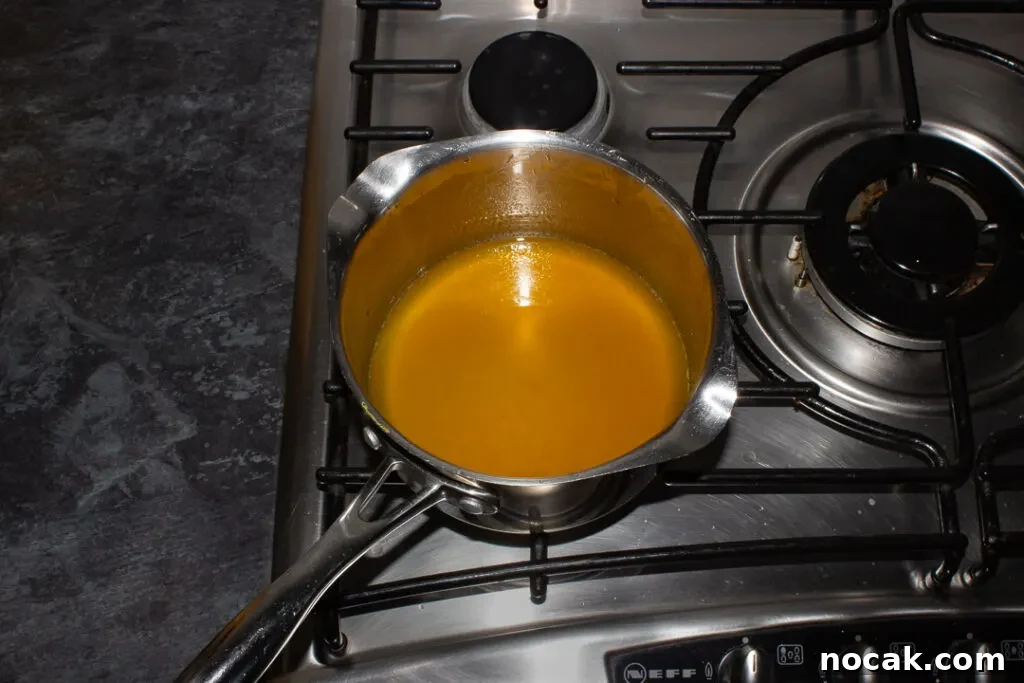 Sticky Orange Glaze Cake Recipe with Zesty Citrus Flavor 12 Orange syrup in a saucepan on the stove top.