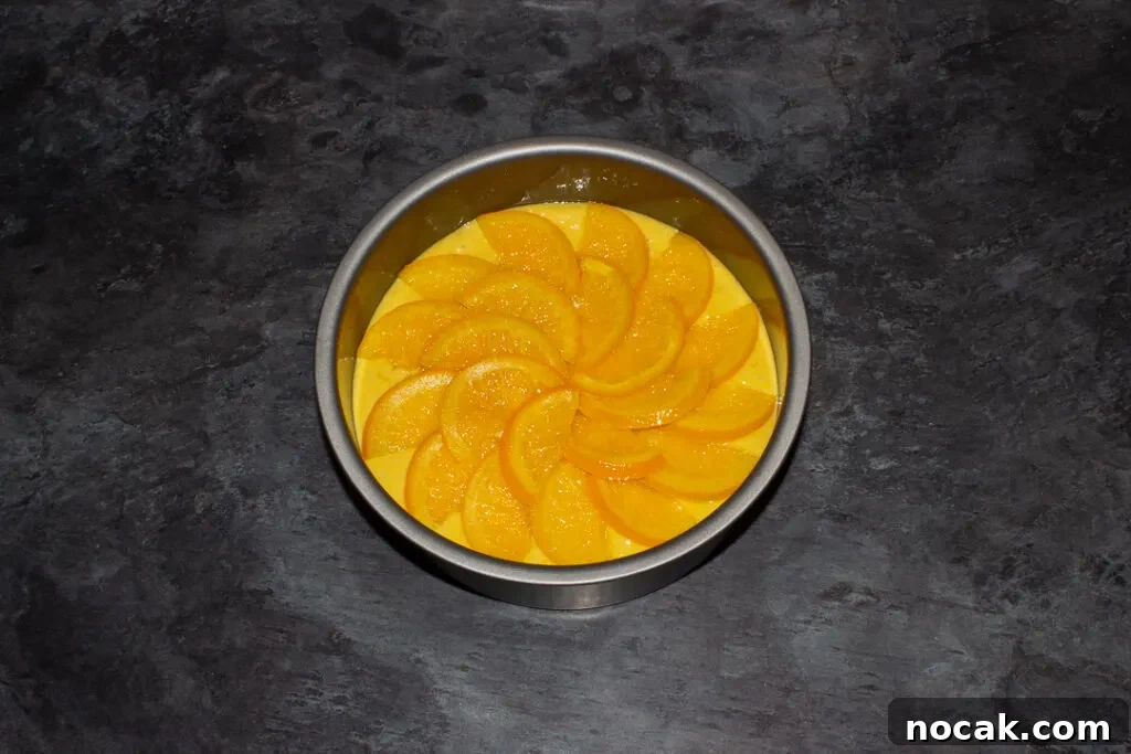 Sticky Orange Glaze Cake Recipe with Zesty Citrus Flavor 15 Sticky orange cake batter topped with orange semicircles in a lined round baking tin on a kitchen worktop.