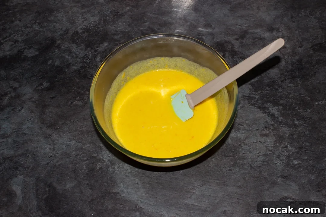 Sticky Orange Glaze Cake Recipe with Zesty Citrus Flavor 26 The wet sticky orange cake ingredients mixed together in a glass bowl with a spatula on a kitchen worktop.