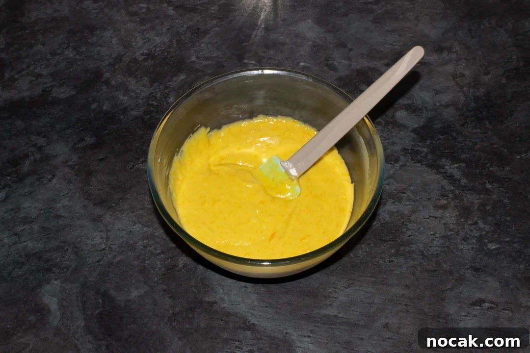 Sticky Orange Glaze Cake Recipe with Zesty Citrus Flavor 28 Sticky orange cake batter in a glass bowl with a spatula on a kitchen worktop.