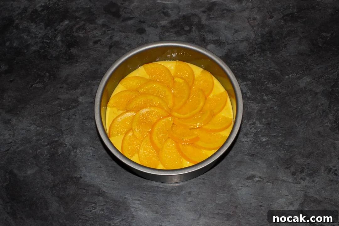 Sticky Orange Glaze Cake Recipe with Zesty Citrus Flavor 29 Sticky orange cake batter topped with orange semicircles in a lined round baking tin on a kitchen worktop.
