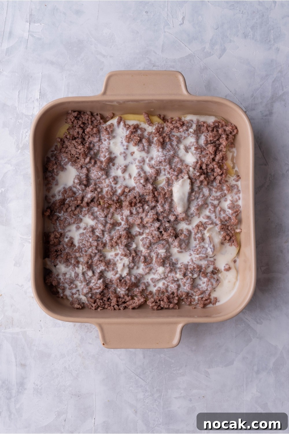 Hearty Hamburger and Potato Casserole with Canned Soup 6 Brown baking dish with layers of cooked ground beef and a creamy sauce mixture.