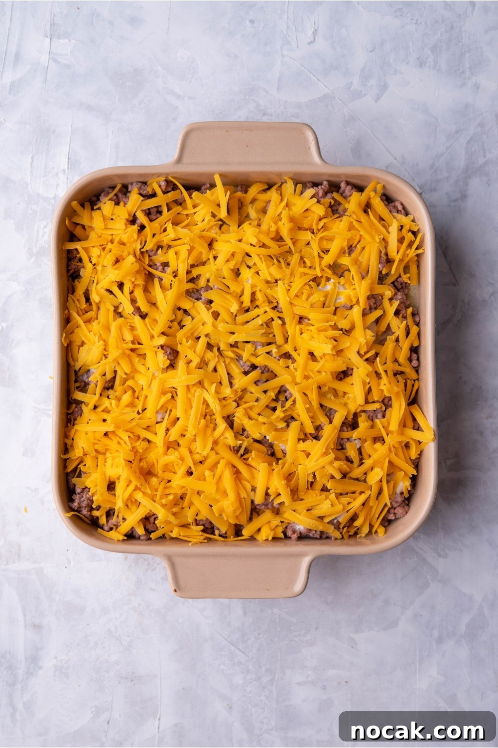 Hearty Hamburger and Potato Casserole with Canned Soup 7 Brown baking dish with unbaked hamburger potato casserole covered in shredded cheese.