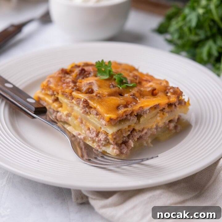 Single serving of hamburger potato casserole on a white plate with a fork on the plate.
