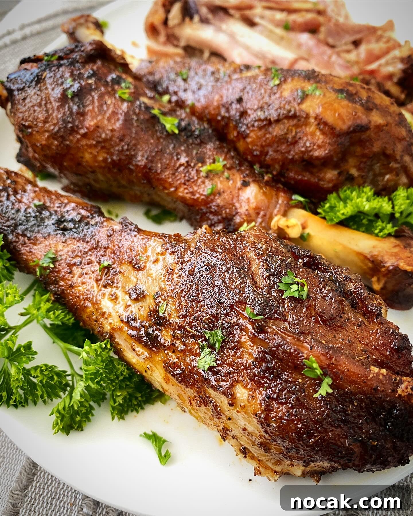 Slow Cooker Turkey Legs Recipe with Step-by-Step Video 7 close up shot of slow cooker turkey legs on a white plate garnished with fresh parsley