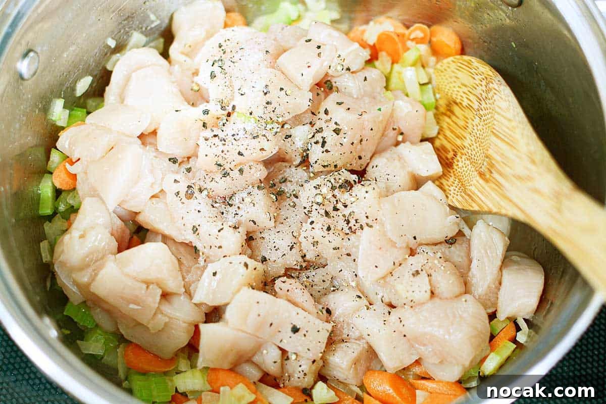 Comforting Chicken and Corn Noodle Soup Recipe 5 raw cubed chicken and vegetables in pot with wooden spoon