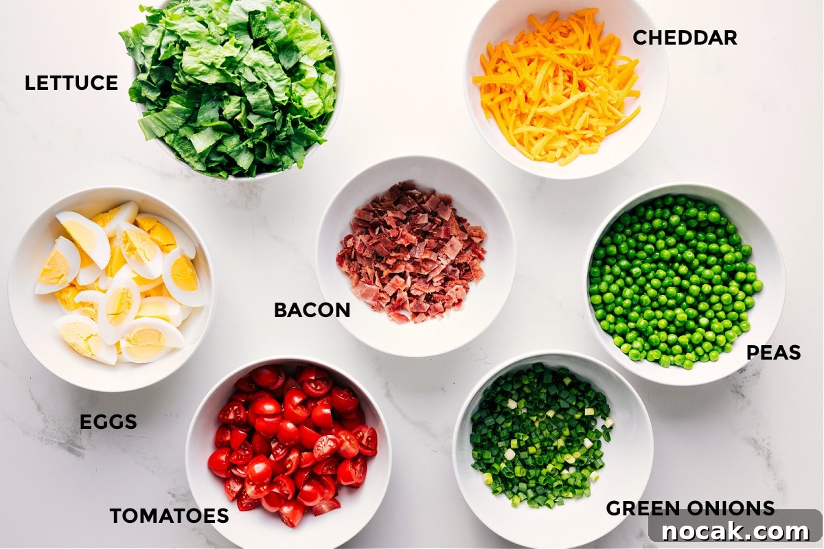 Ingredients In This 7 Layer Salad All the ingredients in this recipe prepped out for easy assembly including the lettuce, eggs, tomatoes, bacon, green onions, peas, and cheddar.