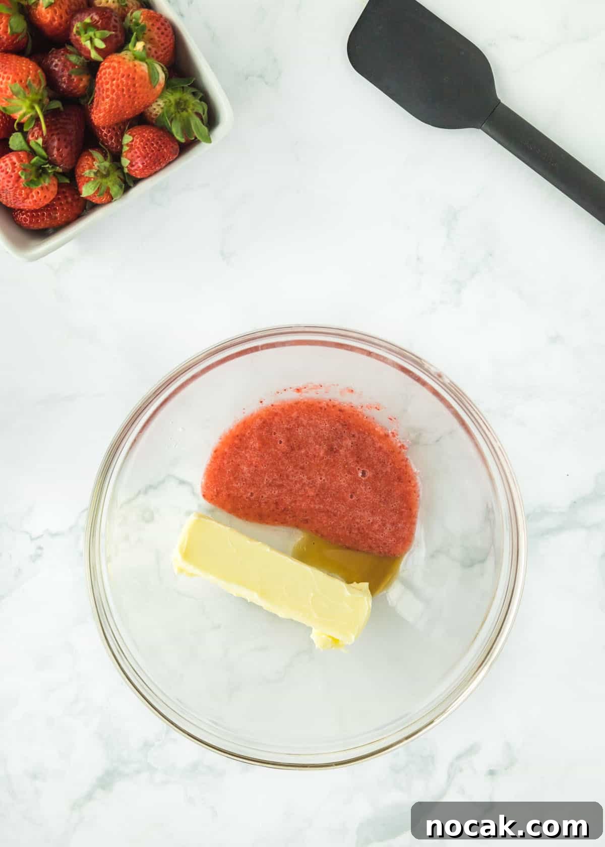 Strawberry Buttercream Frosting Recipe — Smooth, Fresh Flavor 5 Overhead photo of pureed strawberries with one full stick of butter and vanilla. The upper left and right corners are accented with whole strawberries and a black spatula.