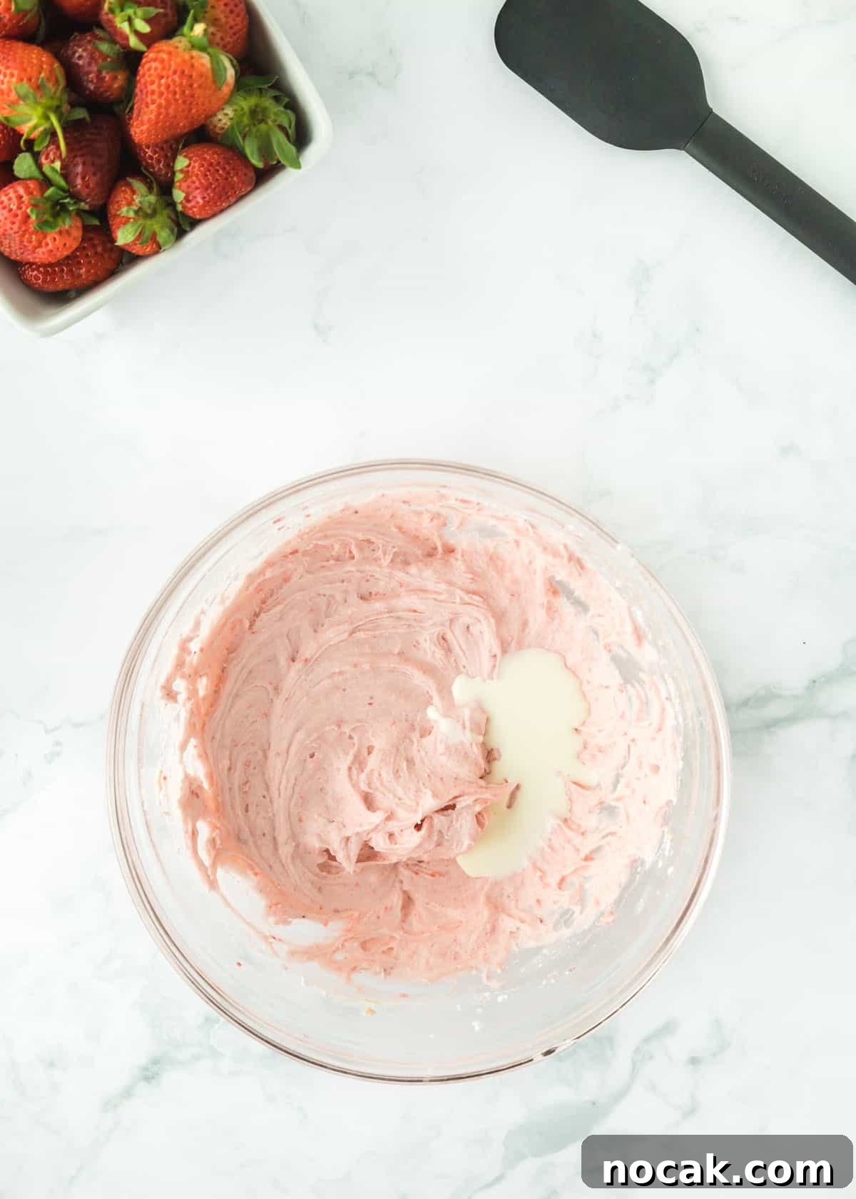 Strawberry Buttercream Frosting Recipe — Smooth, Fresh Flavor 9 Overhead photo of pureed strawberries with one full stick of butter, vanilla, and powdered sugar mixed together with unmixed heavy cream. The upper left and right corners are accented with whole strawberries and a black spatula.