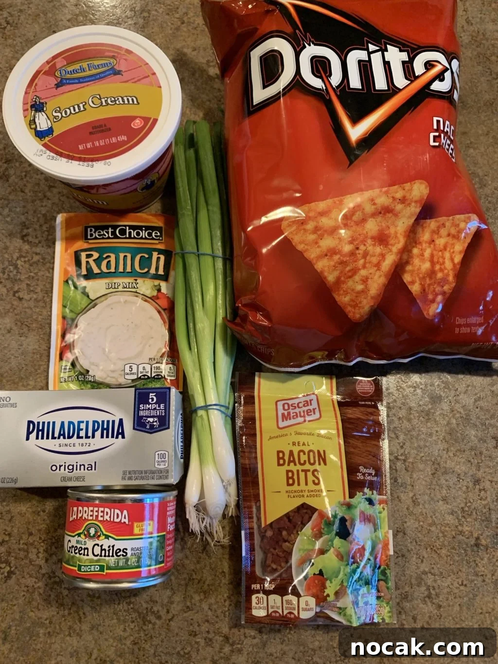 Dorito Dip Recipes: 10 Crowd-Pleasing Dips for Nacho Nights 3 A bag of Nacho Cheese Doritos on a kitchen counter along with the ingredients for the dip, including Sour Cream, Ranch mix, Philadelphia cream cheese, bacon bits, and canned milld green chiles