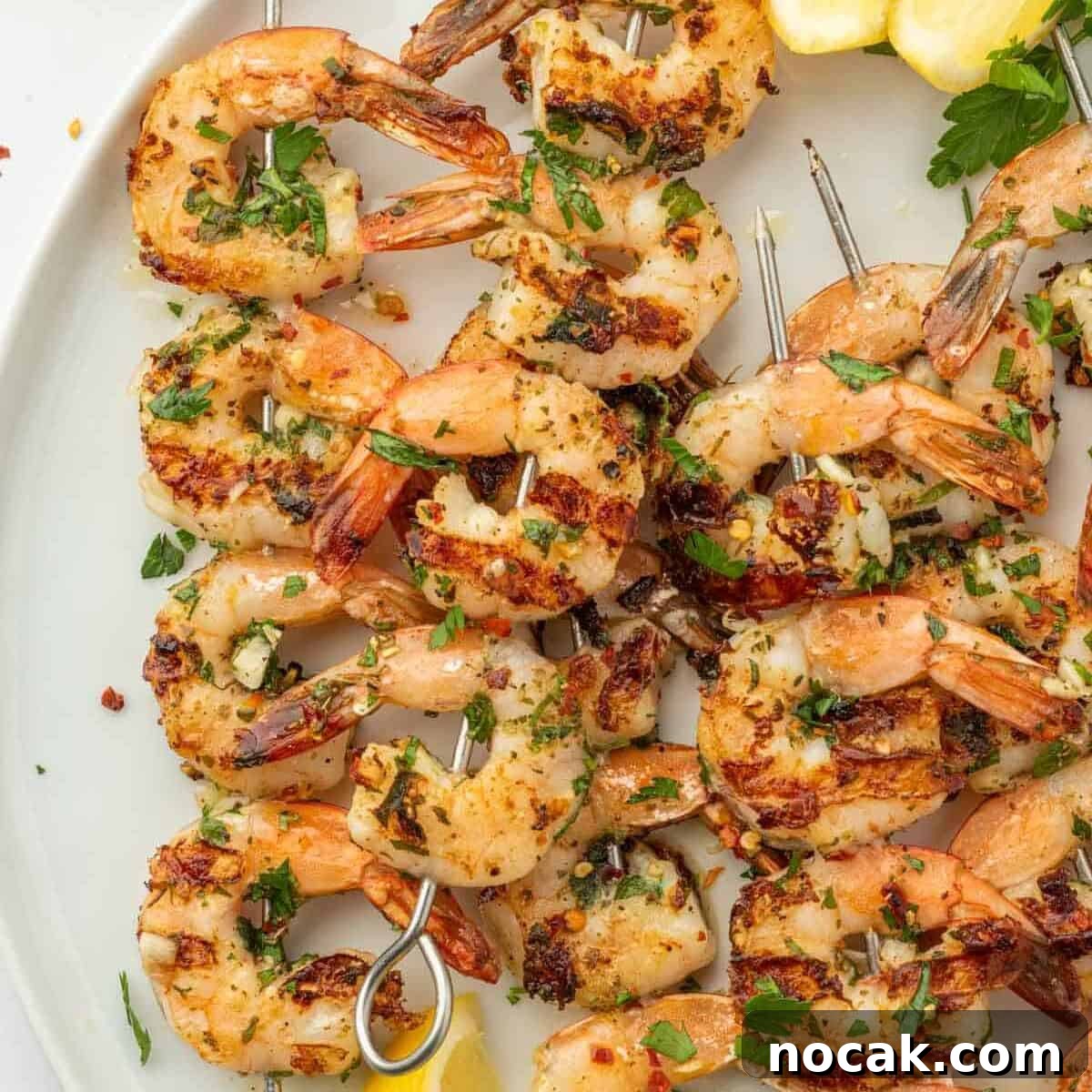 Garlic-Grilled Shrimp Skewers with Zesty Lemon Marinade 7 Shrimp kabobs with garlic on a white platter with lemon wedges.