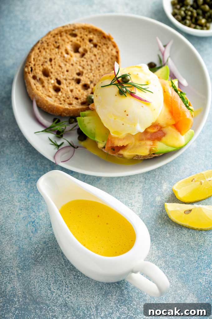 Hollandaise sauce in a white saucer next to a plate with Eggs Benedict.