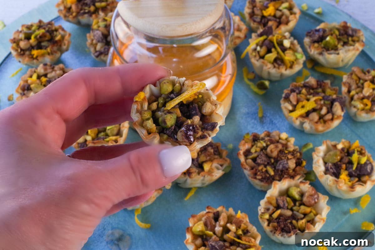 Hand holding up Chocolate Baklava Bite with honey and more Baklava Bites in the background.