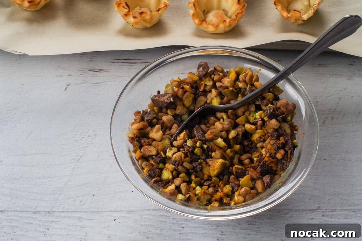 The chopped pistachios, walnuts, chopped chocolate, cinnamon, and orange zest stirred together in a small glass bowl with a spoon.