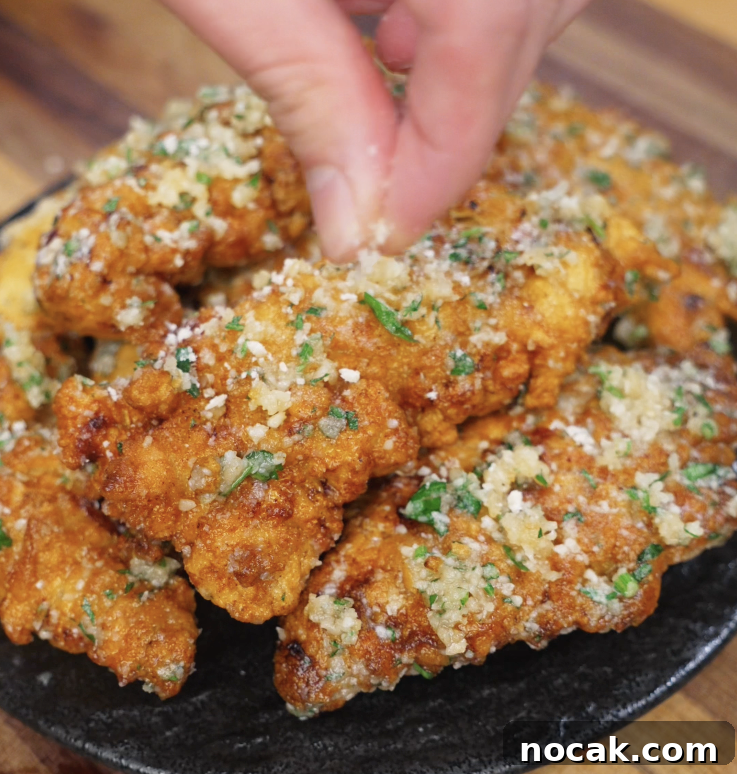 Crispy Garlic Parmesan Chicken Tenders Recipe 9 A hand sprinkles extra parmesan over a plate of garlic parmesan chicken tenders, finishing them with cheesy, herby flair.