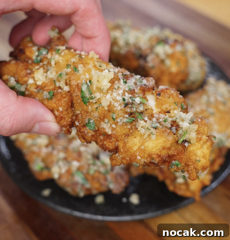 Crispy Garlic Parmesan Chicken Tenders Recipe 3 A single garlic parmesan chicken tender is held up to the camera, showing its crispy coating glistening with garlic butter and cheese.