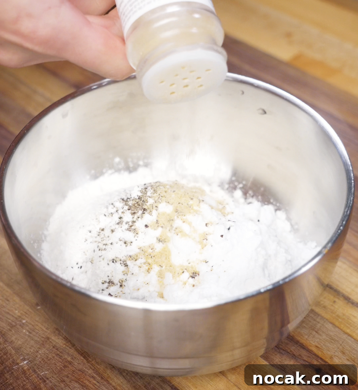 Crispy Garlic Parmesan Chicken Tenders Recipe 5 Garlic powder is shaken into a bowl of flour, potato starch, salt, and pepper to season the dry dredge for crispy chicken tenders.