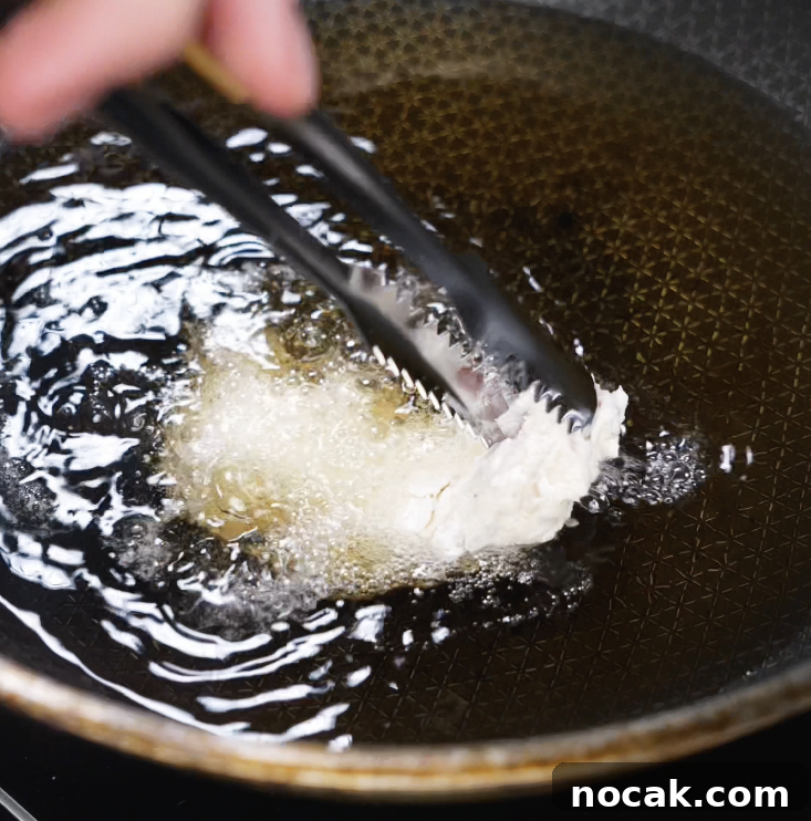 Crispy Garlic Parmesan Chicken Tenders Recipe 6 A pair of tongs gently lowers a battered chicken tender into hot oil, starting the deep-frying process until golden and crispy.