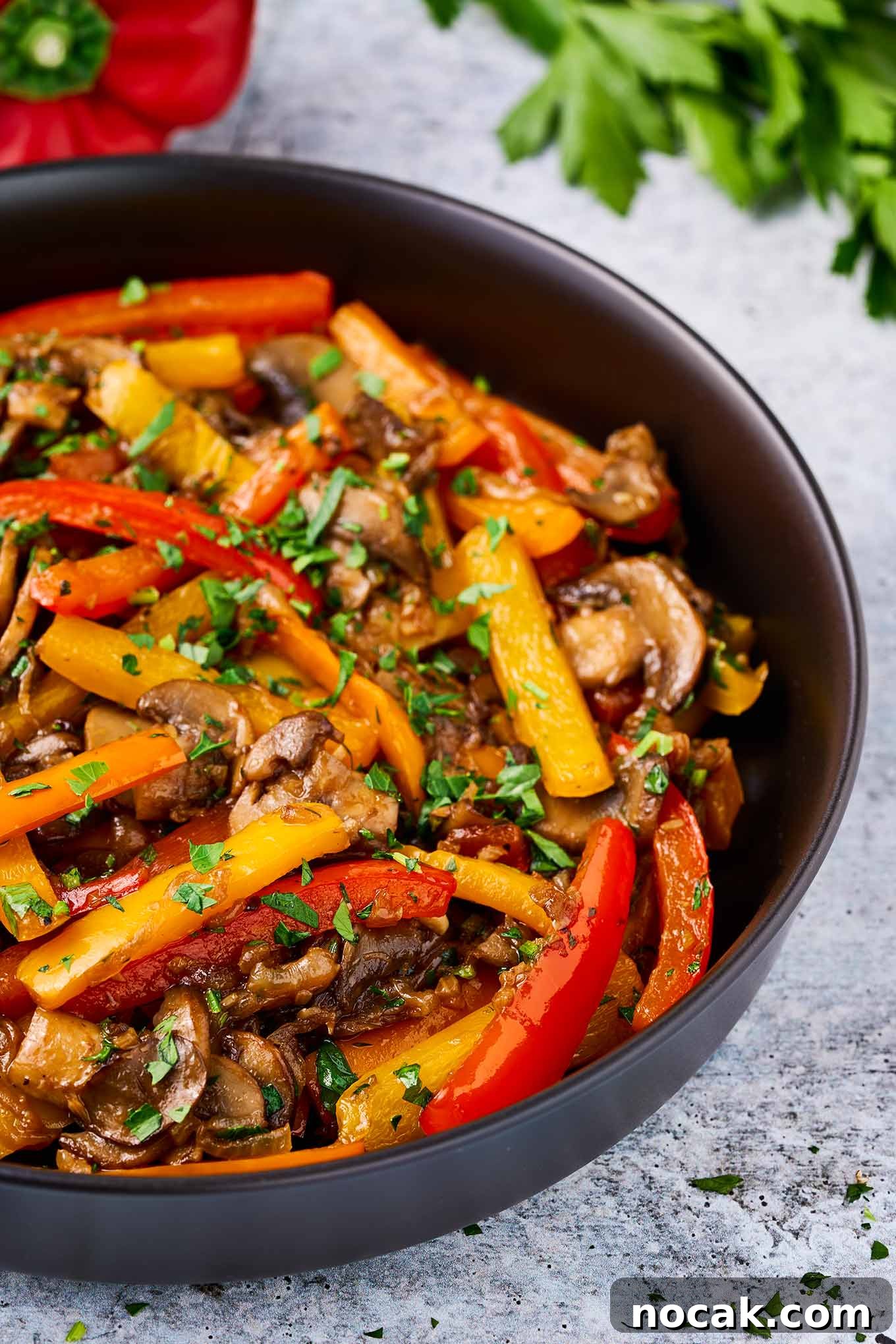 Sautéed Peppers, Mushrooms & Onions Recipe for Flavorful Sides 5 Sautéed vegetables in a black bowl: colorful mix of bell peppers, mushrooms, and onions topped with fresh parsley.