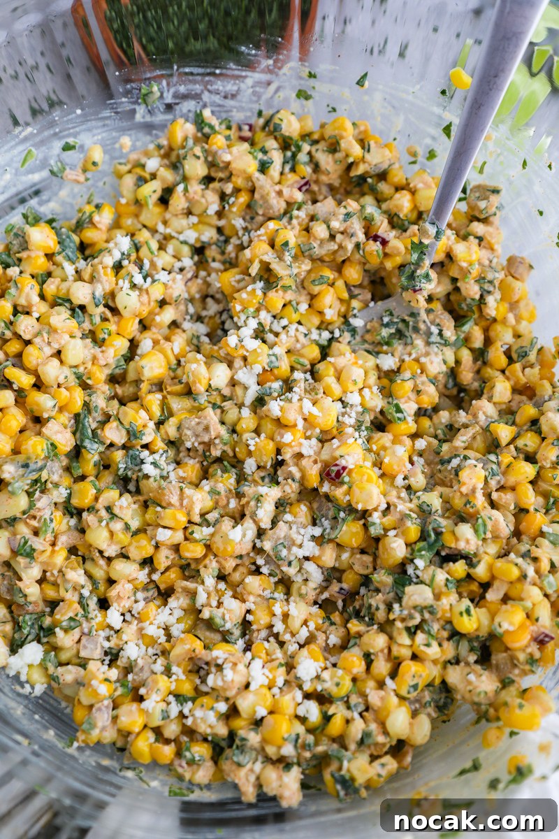 Mexican Street Corn Dip Recipe: Creamy Elote-Inspired Dip 5 A large clear mixing bowl filled with freshly made elote dip (Mexican street corn) with a serving spoon digging into it