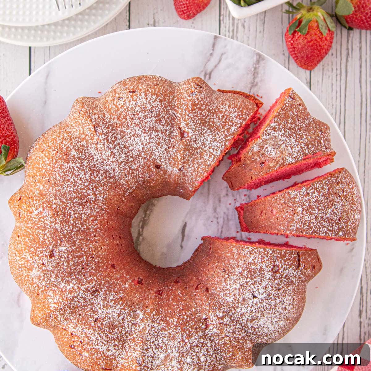 Old-Fashioned Strawberry Pound Cake with Cream Cheese Frosting 4 A marble plate displays a strawberry bundt cake with 2 slices cut to show the red cake color.