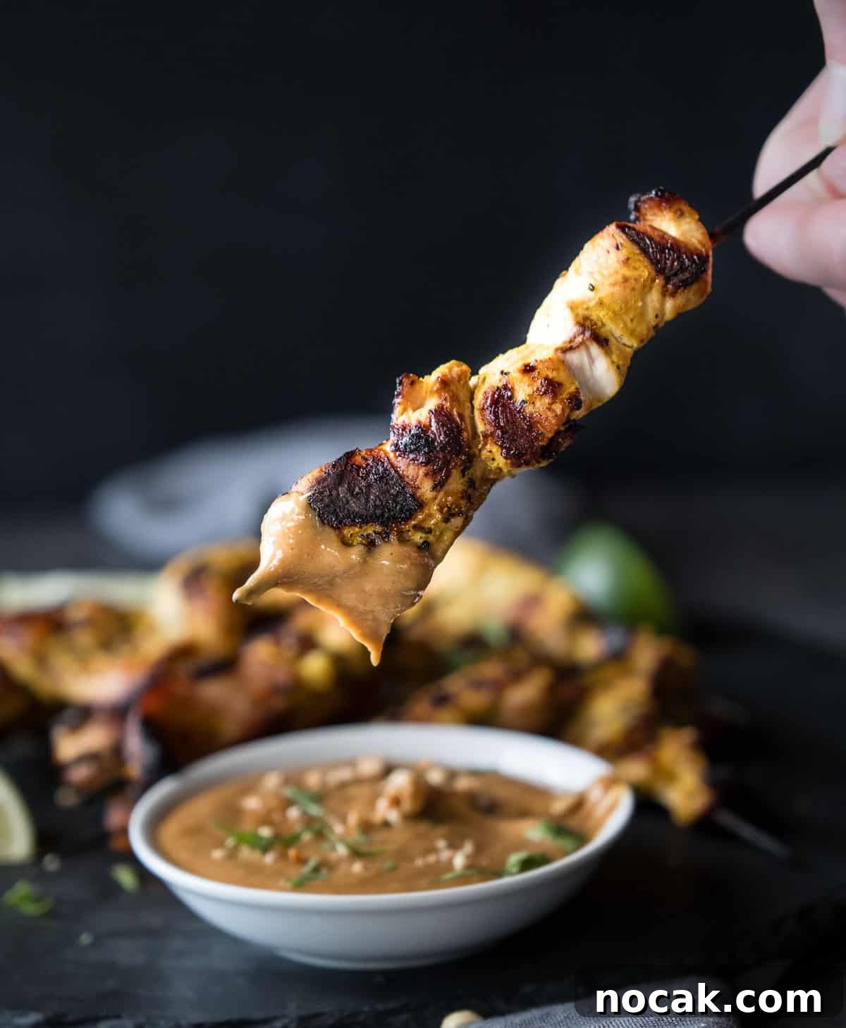 Chicken Satay Skewers with Creamy Peanut Dipping Sauce 7 Mary from Vindulge holding a chicken satay skewer after dipping in peanut sauce.