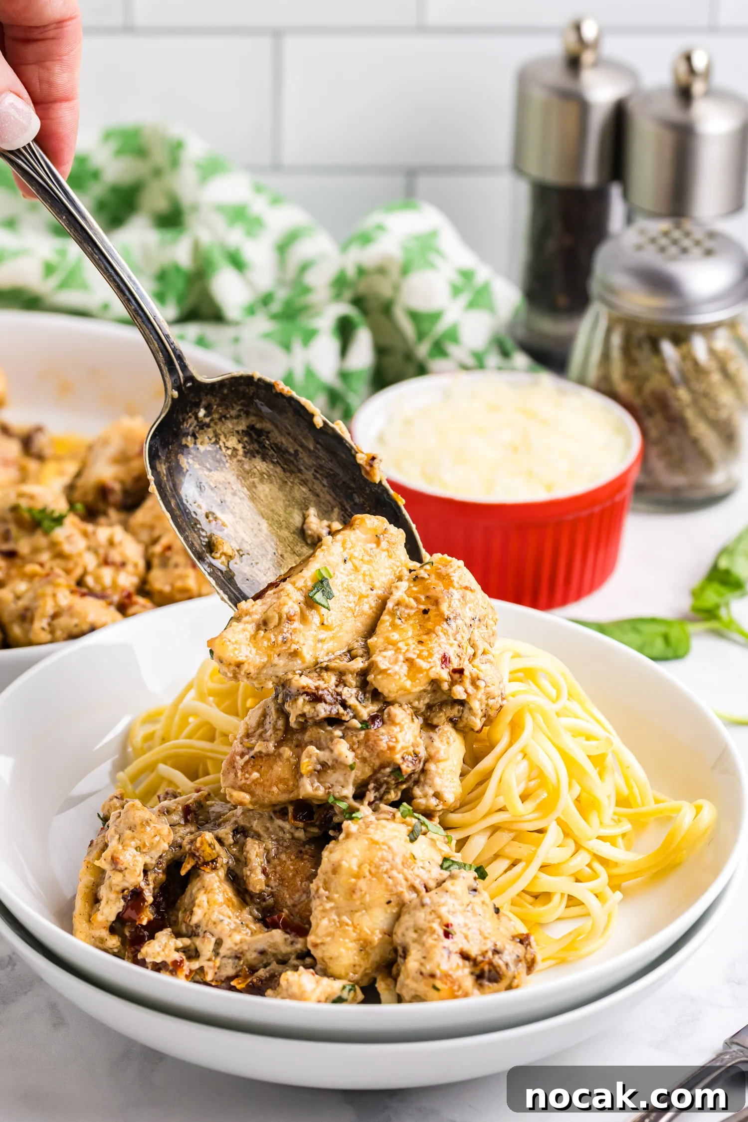 Blackstone Marry Me Chicken Recipe: Skillet Chicken with Creamy Sun-Dried Tomato Sauce 2 A spoon lifts creamy sun-dried tomato chicken over a bowl of cooked pasta, with grated cheese and seasonings visible in the background.