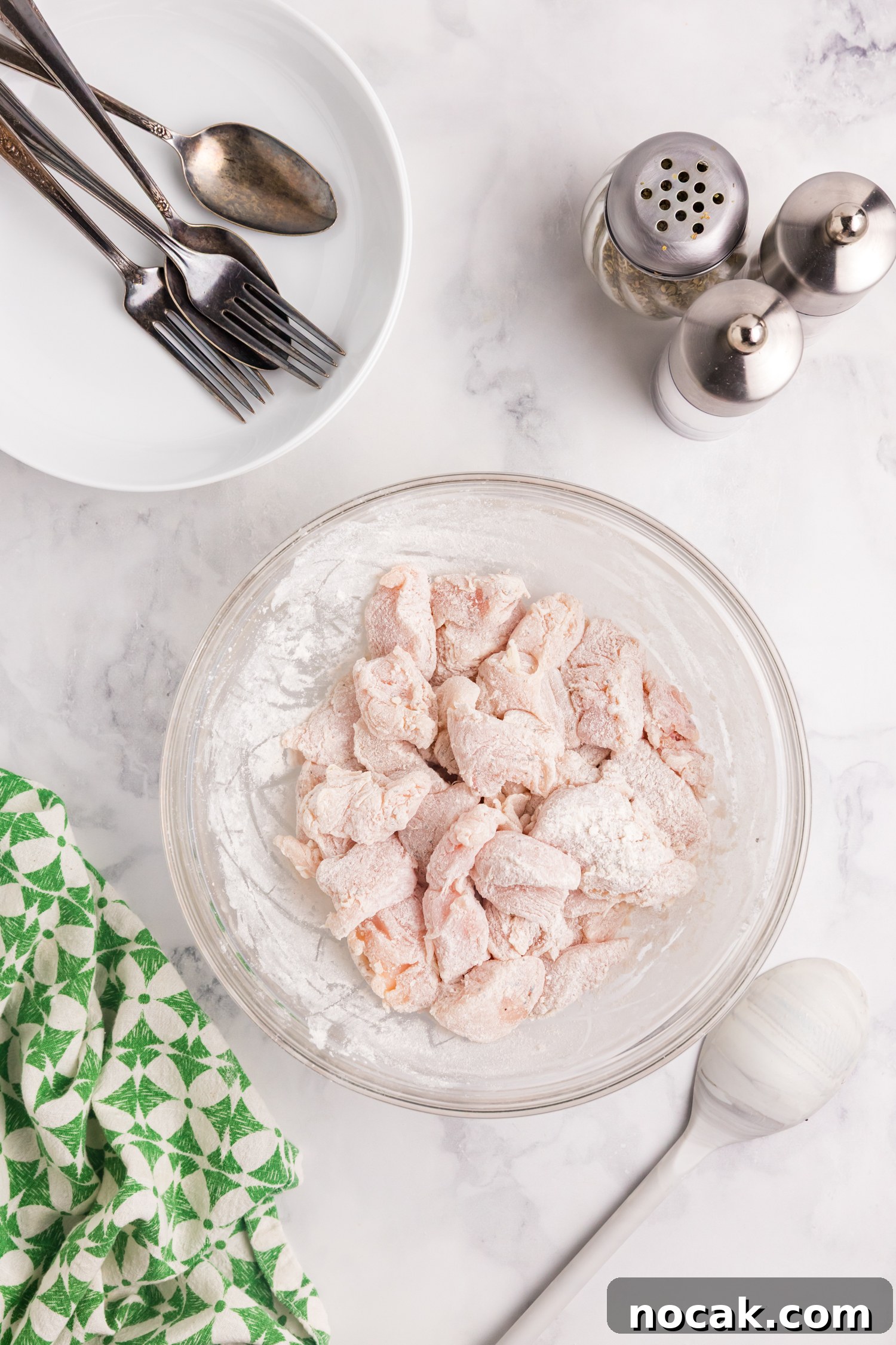 Blackstone Marry Me Chicken Recipe: Skillet Chicken with Creamy Sun-Dried Tomato Sauce 4 Raw chicken pieces coated in flour sit in a glass bowl on a marble countertop.