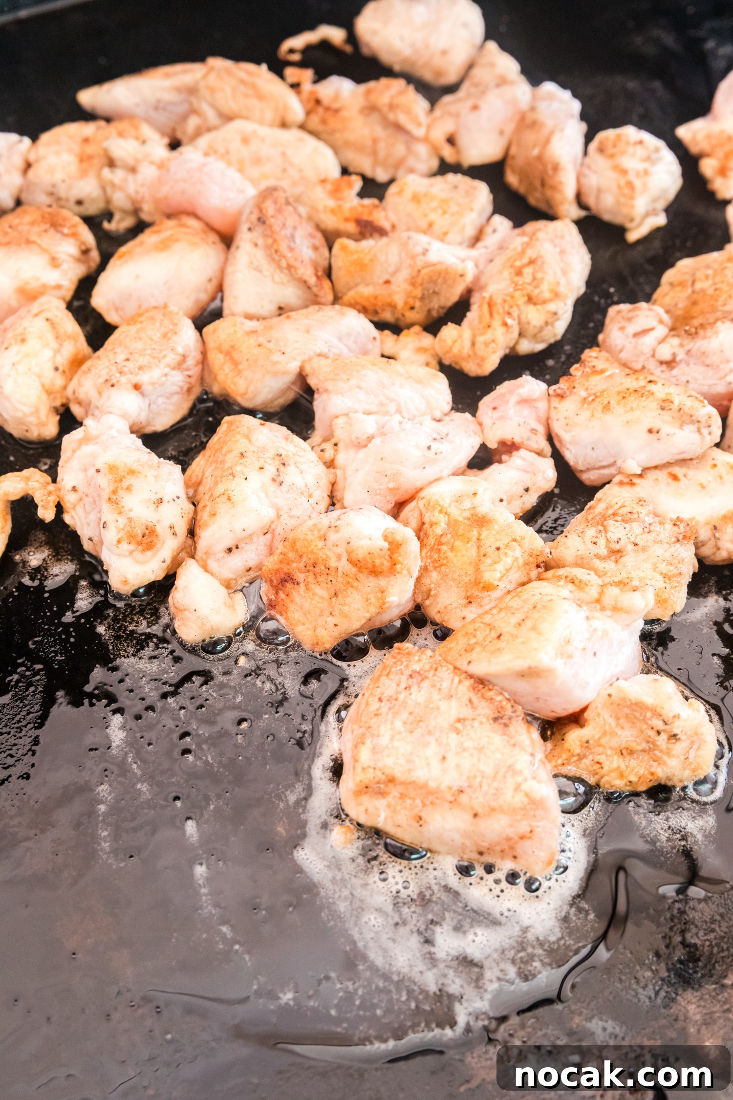 Blackstone Marry Me Chicken Recipe: Skillet Chicken with Creamy Sun-Dried Tomato Sauce 5 Bite-sized chicken pieces cook on a flat-top griddle, lightly browned on the outside with oil bubbling around them.