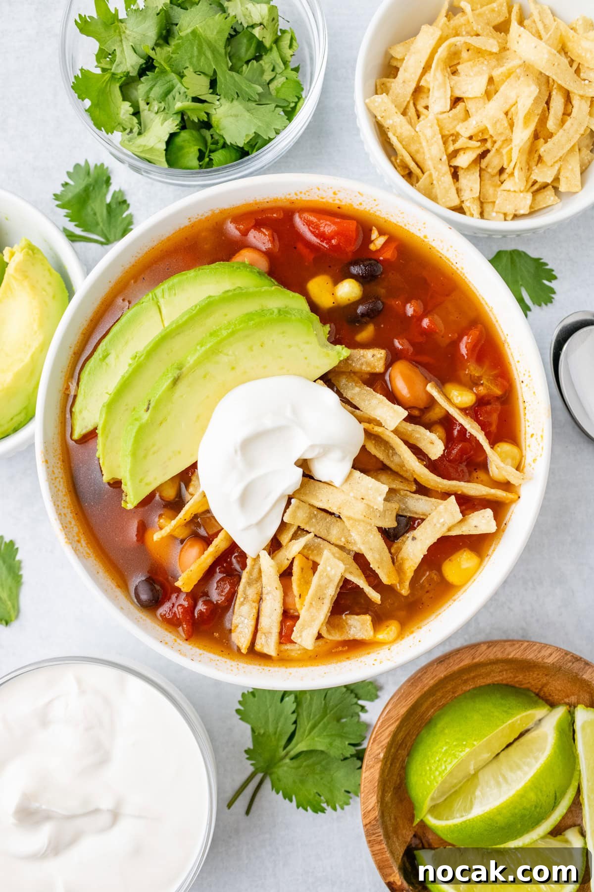 An overhead image of slow cooker tortilla soup in a bowl with avocado slices and sour cream on top.
