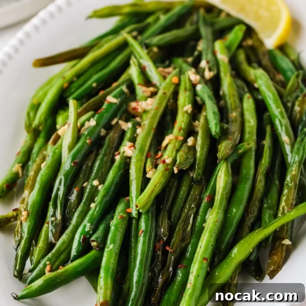 Close-up of skillet green beans with garlic, red pepper flakes, and lemon wedges on a serving platter.