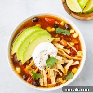 An overhead image of slow cooker tortilla soup in a bowl with avocado slices and sour cream on top.